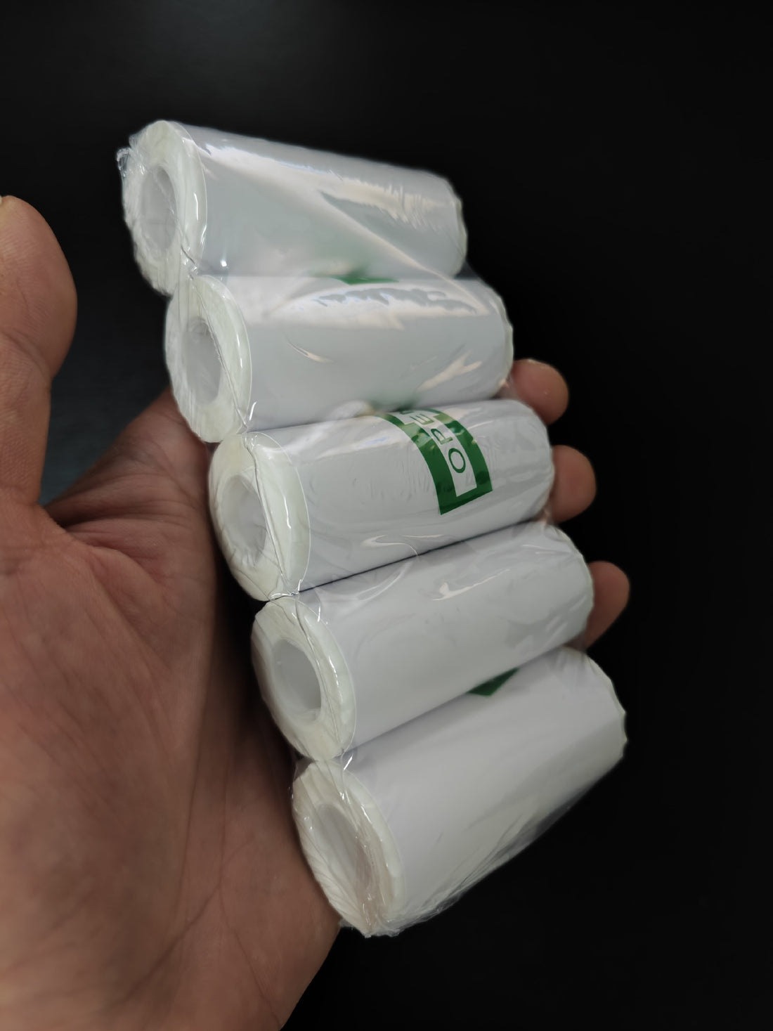Hand holding five rolls of white paper with green labels against a black background