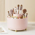 Pink makeup brush holder with various brushes and products on a light background