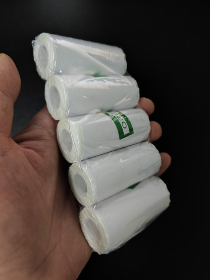 Hand holding five rolls of white paper with green labels against a black background