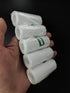 Hand holding five rolls of white paper with green labels against a black background