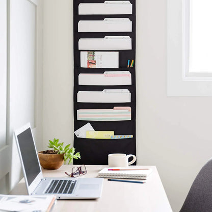 Wall-mounted file organizer with folders on a white wall above a desk with office supplies.